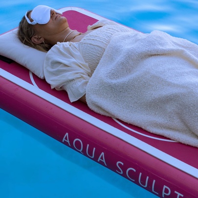 Person lying on a floating bed on a pool, with eye mask and pillow.