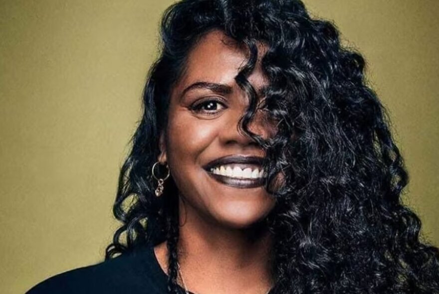 Woman smiling with long black ringlets half-hiding her face.