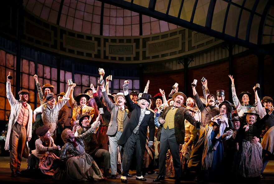 A scene from the musical My Fair Lady, with a large ensemble cast singing and dancing on stage.