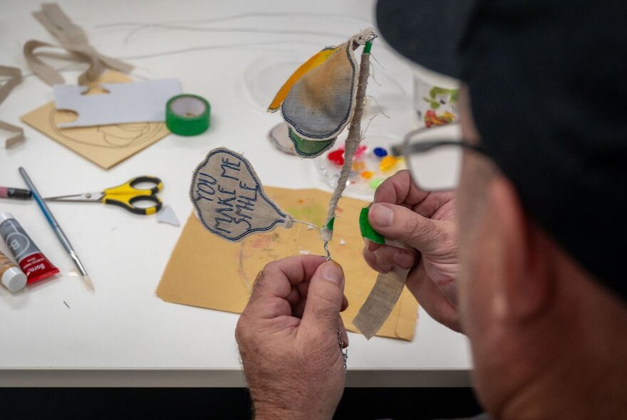 Close-up of a person's hands working on a paper craft project at a table with various art supplies.