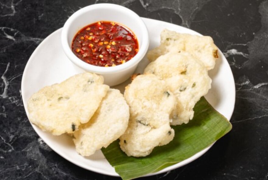 Fried puffs on a plate with a bowl of chilli sauce.