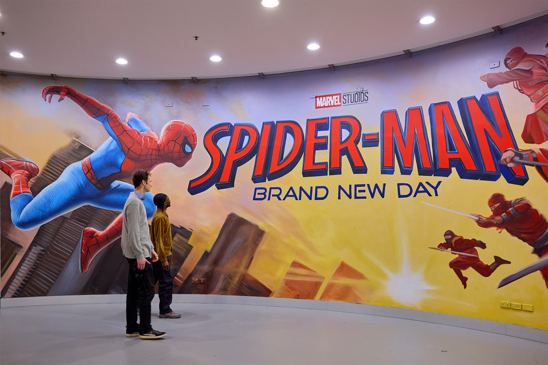 Two people are walking past a large spider man movie poster