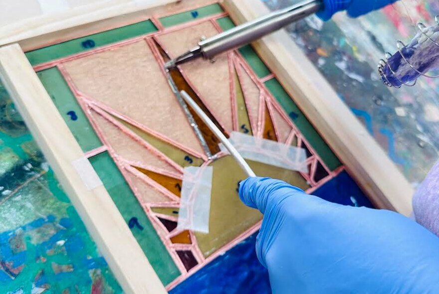 Gloved hands using tools to create a leadlight glass window.