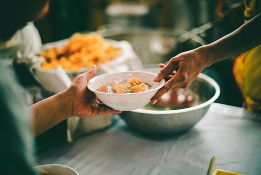 An outstretched hand offers a bowl of food to another hand. 