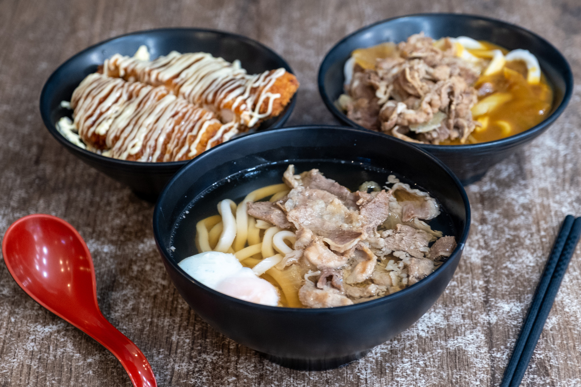 Three bowls of different types of udon noodles including curry, beef and egg and tempura with mayonnaise on top 