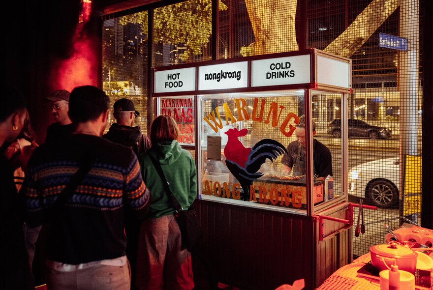 A food cart at night, with people lined up in front of it waiting to buy food.