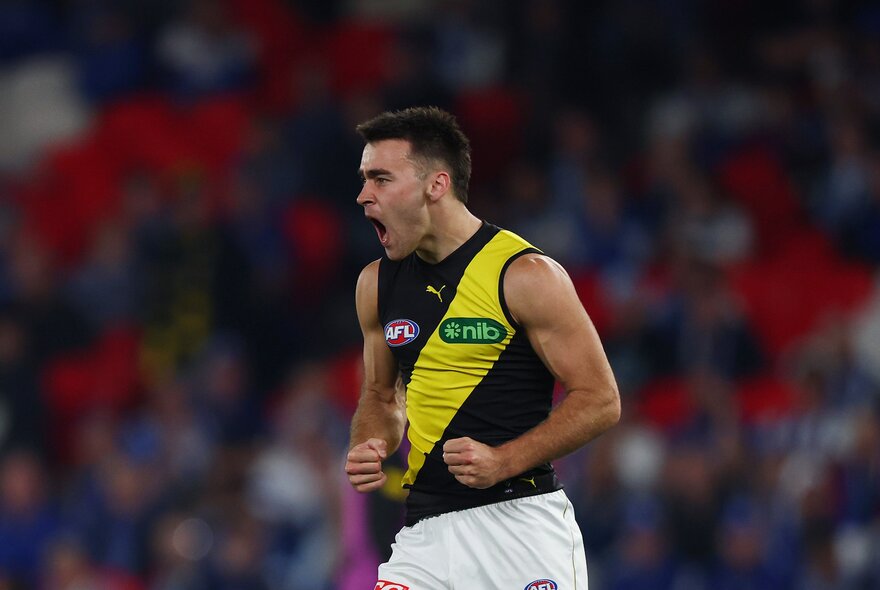 A cheering Richmond AFL football player with clenched fists on the field during a match.