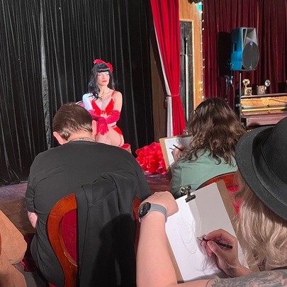 A burlesque life drawing class with a sitter up front in a red dress. 