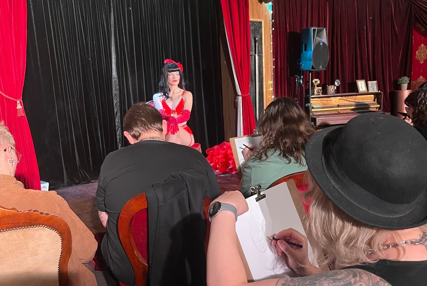 A burlesque life drawing class with a sitter up front in a red dress. 