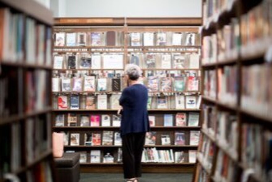 A person perusing books on shelves in Melbourne Athenaeum Library.