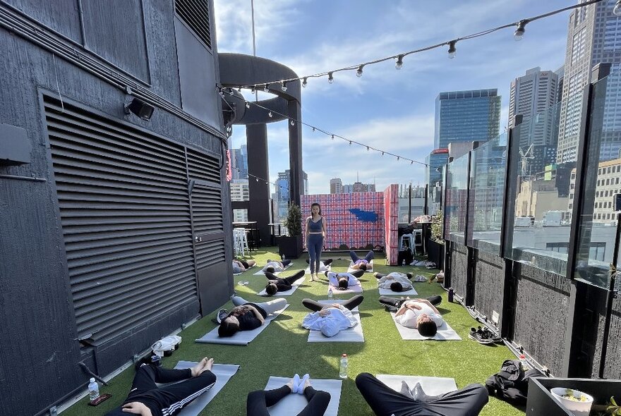 People doing yoga on mats on an outdoor rooftop with city views.