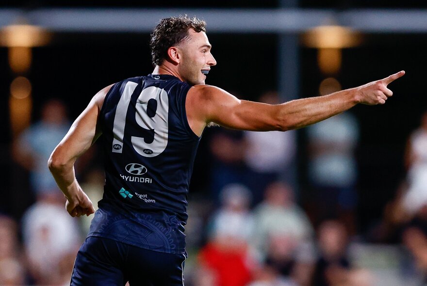A Carlton AFL football player with one arm outstretched during a match.