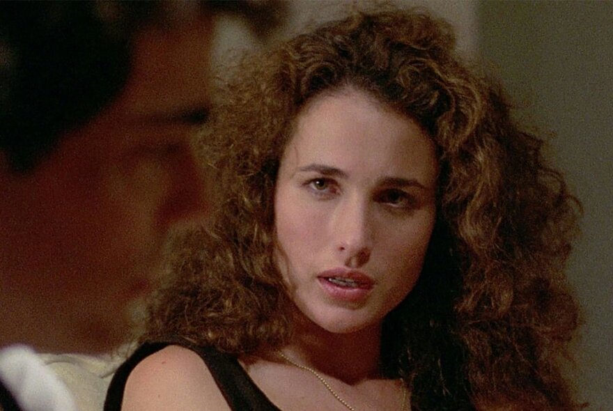Film still of the face of actress Andie MacDowell, her long curly hair framing her face. 
