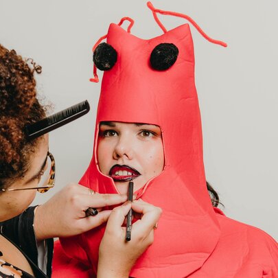 A make-up artist applying lipstick to a woman dressed in a lobster costume.                                                                                                                                                                                                                                                                                                     