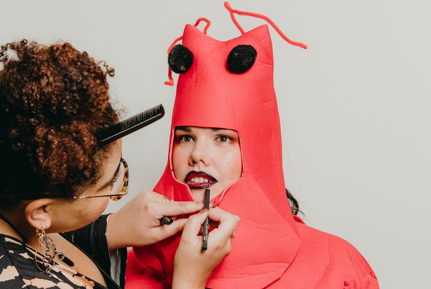 A make-up artist applying lipstick to a woman dressed in a lobster costume.                                                                                                                                                                                                                                                                                                     