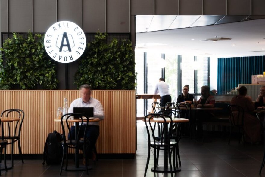 The modern fit out at Axil Coffee Galleria, with a person seated at a table having a coffee with his laptop open, more people in the background.