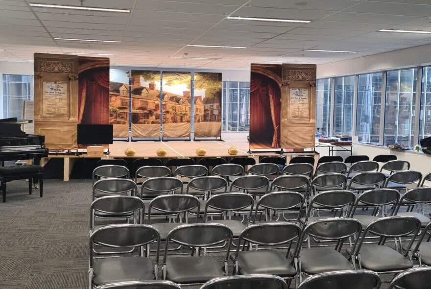 Rows of chairs facing a small stage inside a large room in an office building, a grand piano near the stage.