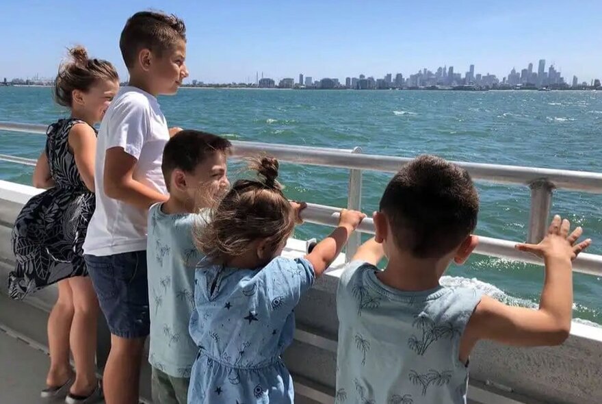 A group of children looking out at the Melbourne skyline from a ferry vessel crossing Port Phillip Bay.