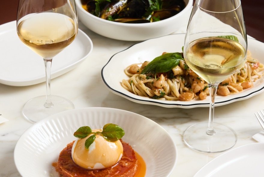 A selection of delicious Italian food, including a pasta dish, a mozzarella dish and two glasses of white wine.
