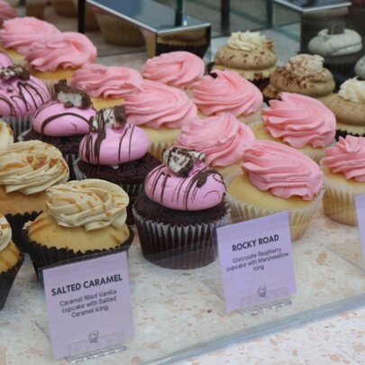 Rows of cupcakes with different icing flavours on a counter behind labels.