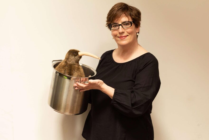 A woman in a black top holding a kiwi in an ice bucket. 