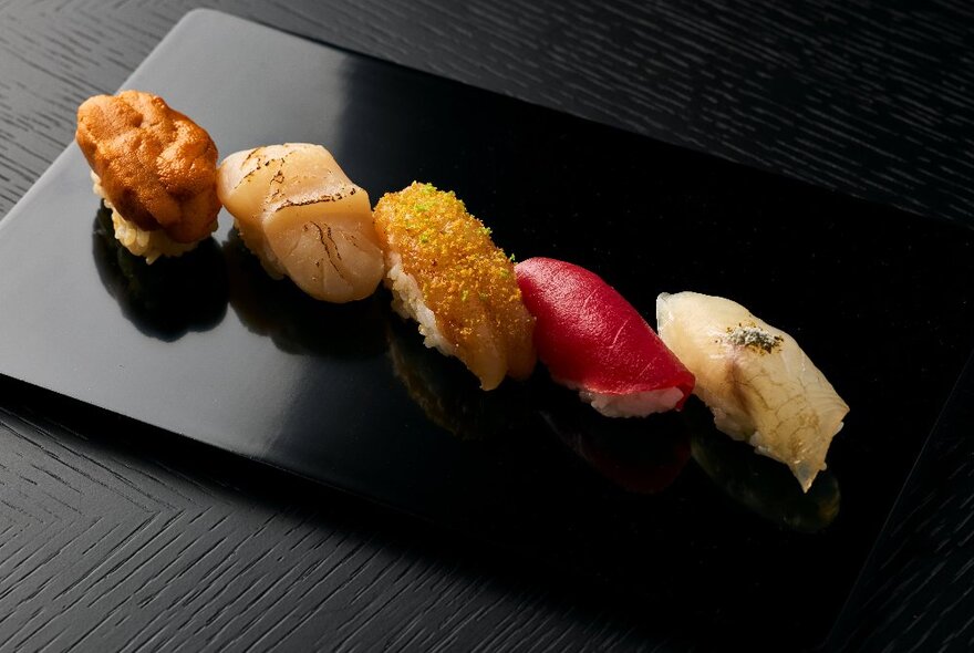 A black rectangular plate featuring five pieces of  sushi.