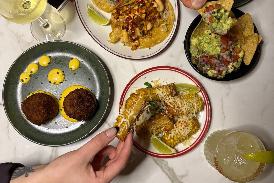 A hand selecting food from a small snack plate, with several other plates of food on the table.