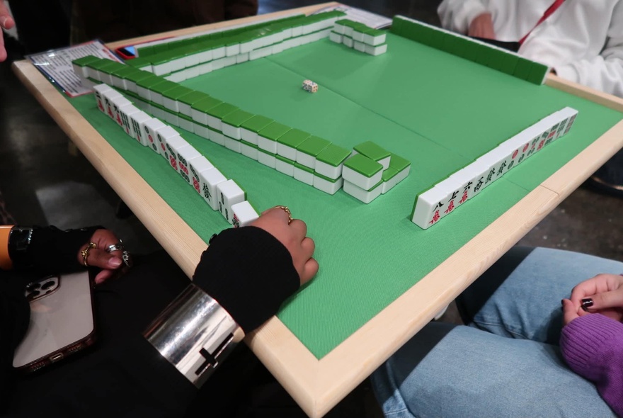 A green mahjong table with lines of tiles, people sitting around the table playing the game.