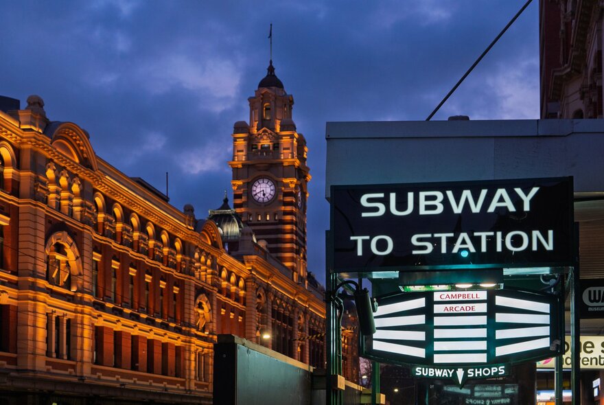 The exterior of the subway entry to Campbell Arcade from Flinders Street, the station illuminated at night in the background. 