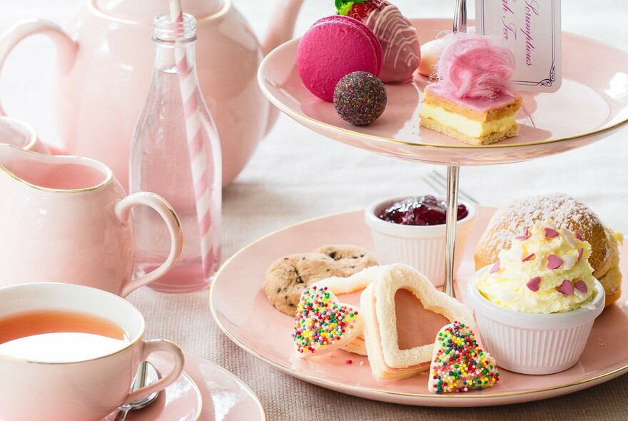 Pink tea cup, jug and teapot with cake stand with petits-fours, jam and biscuits.