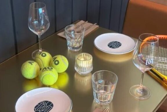 A bronze coloured table set for two with four tennis balls and a tennis racquet also on the table.