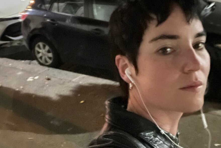 Young woman wearing earbuds, standing in front of a car