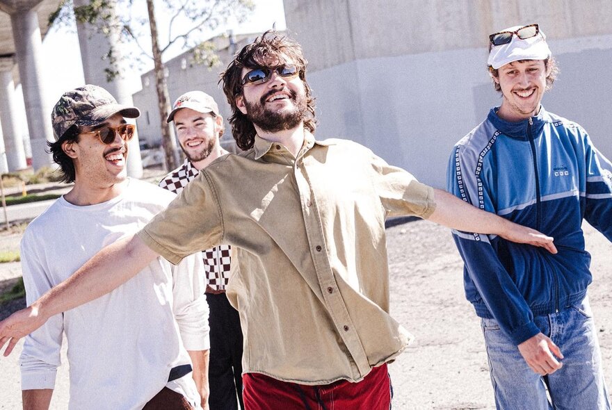A group of men out in the sunshine, the one at the front with his arms outstretched, all smiling and looking carefree.