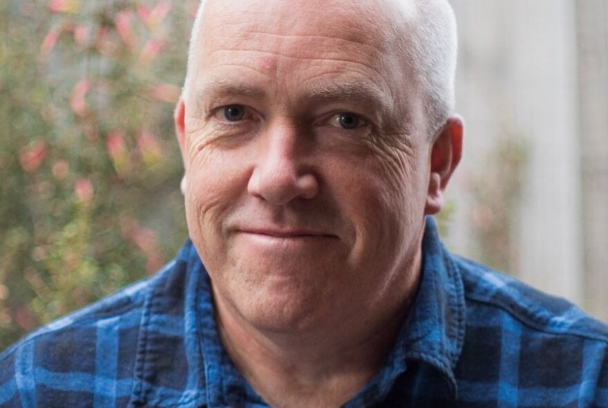 Author Michael Winkler, a middle-aged bald man smiling at the camera, wearing a blue and black check shirt.