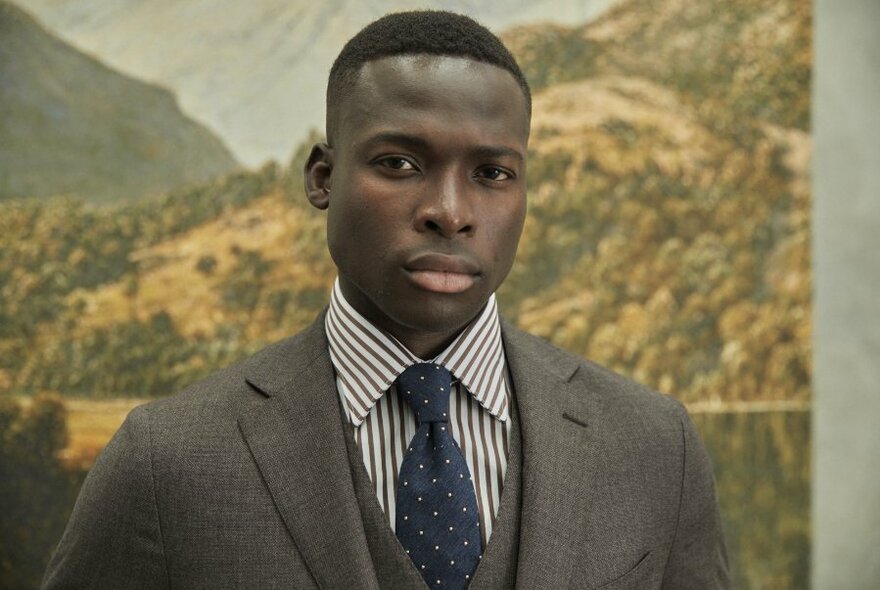 A male model with a grey suit, vest, striped shirt and blue tie.