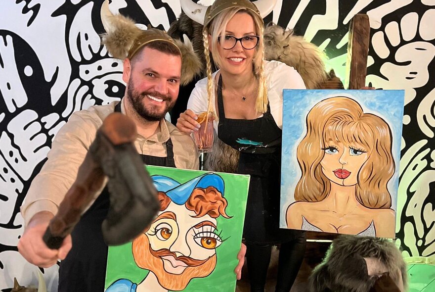 Two people holding painted portraits of each other, one also holding an axe.