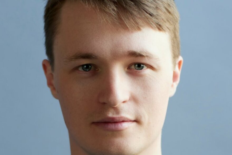 Portrait of Neuroscientist, Ariel Zeleznikow-Johnston, with a neutral expression, in front of a pale blue background.
