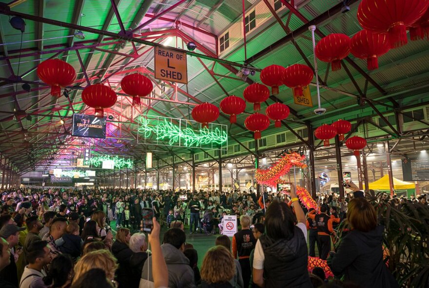 People crowded in the Queen Victoria Market with red lanterns overhead.