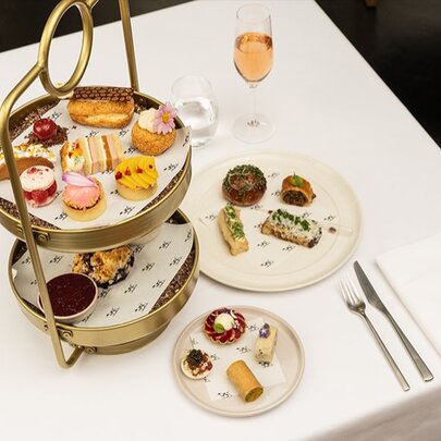 A gold two-tiered cake stand alongside two small white plates, all filled with a selection of small delicacies.