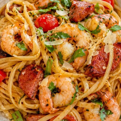 A bowl of pasta with prawns and cherry tomatoes. 