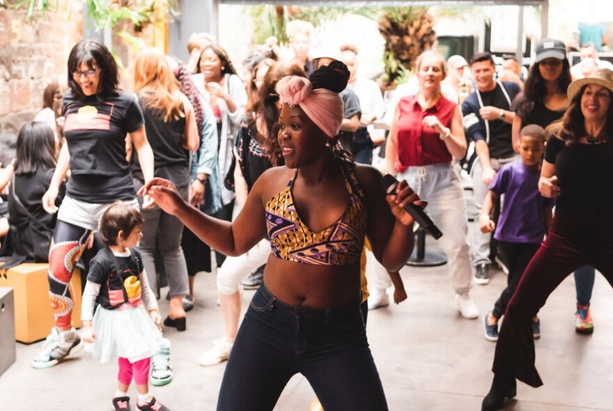 Adults and children dancing with an African dancer in a courtyard space.