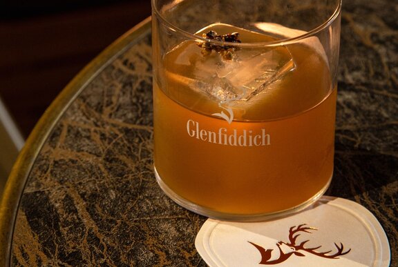 A glass of Glenfiddich whisky on a coaster on a marble table top.