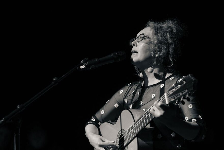 Singer strumming a guitar in the dark.