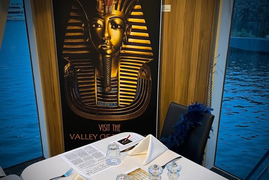 A table set with napkins and cutlery, with printed flyers on each place setting, and a large poster of Tutankhamun's gold face mask in the background.