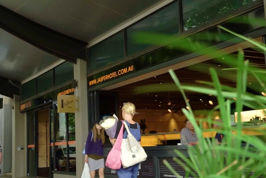 Green plants in foreground with people queuing at open window and counter.