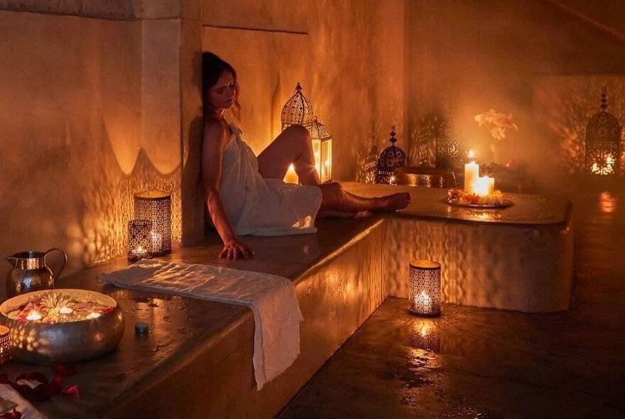 A woman seated in a candlelit spa setting.