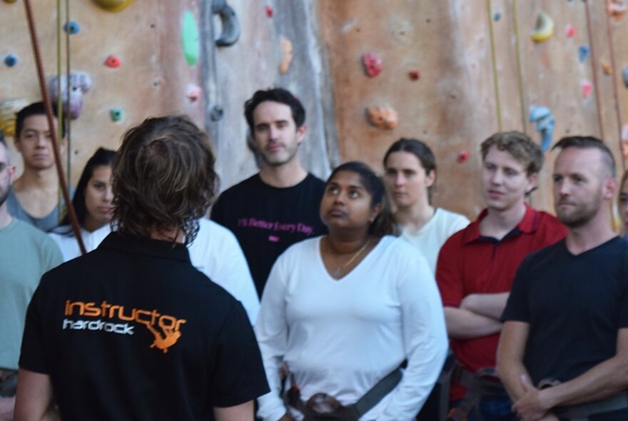 An instructor talking to a group of people before they start indoor climbing, the climbing wall in the background.