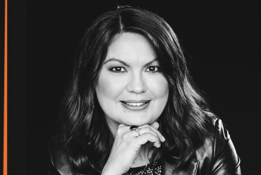 A black and white headshot of author Katya de Becerra, smiling while resting her chin on her right hand.