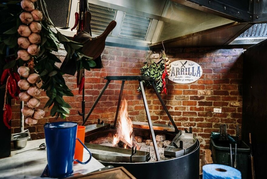 Open barbecue grill in brick-lined space with hanging strings of garlic.