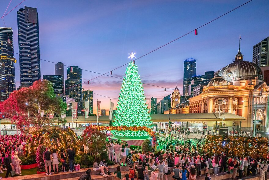 A giant green LED Christmas tree in the city surrounded by crowds.